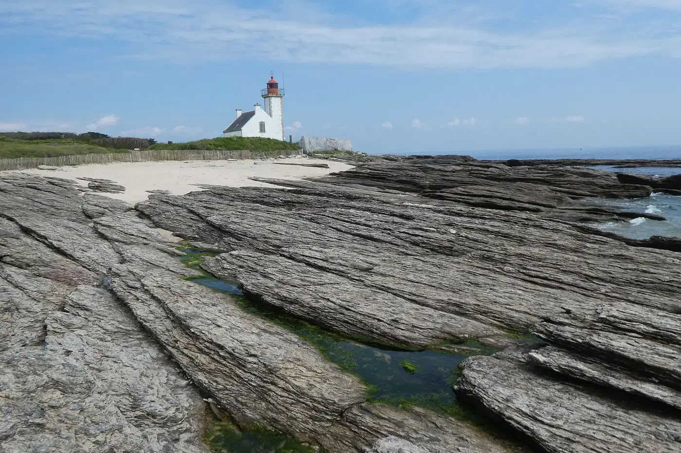Platier de roches feuilletées à la pointe des Chats, avec le phare blanc et rouge au fond