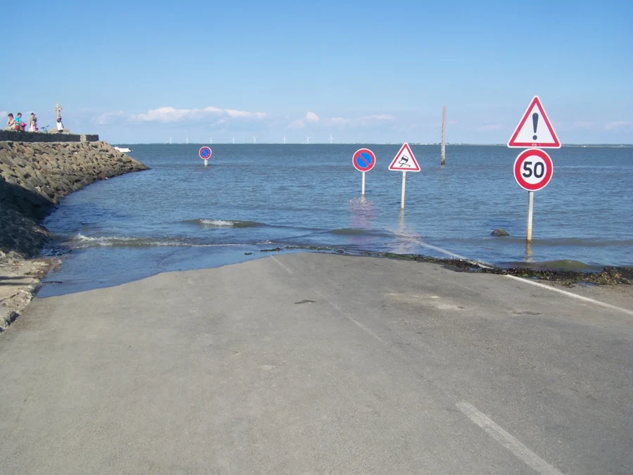 Passage du Gois recouvert par la marée montante, panneaux de signalisation émergeant de l'eau