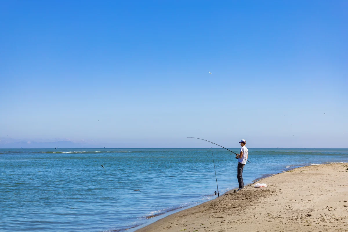 Pêcheur tenant une canne depuis une plage au bord de la mer