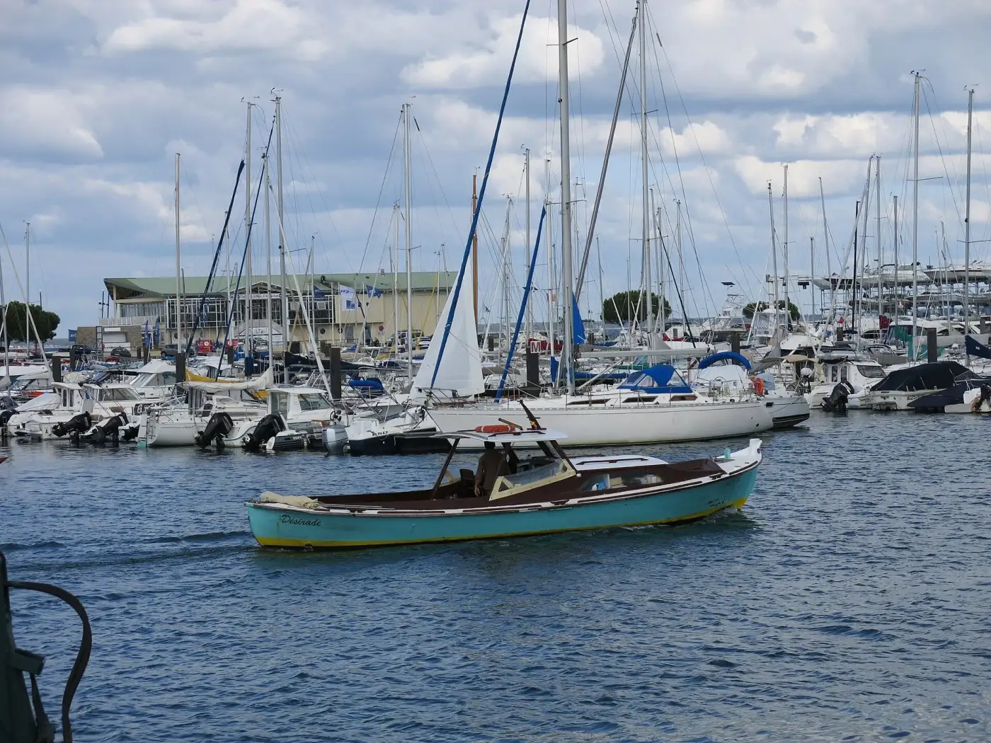Pinasse en bois bleue naviguant devant les voiliers amarrés du port d'Arcachon